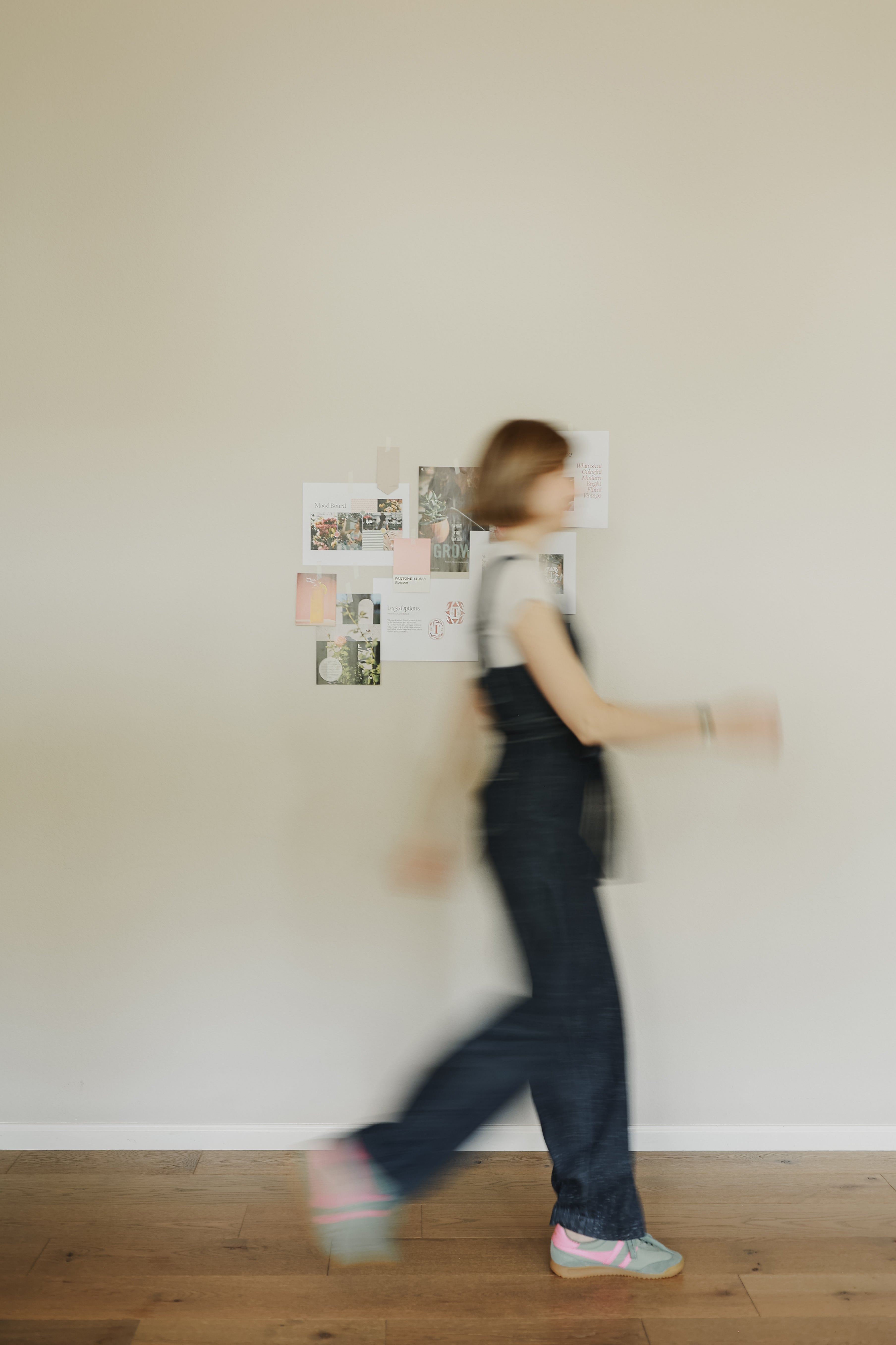 Person walking past a wall with pinned photos in a minimalistic room.