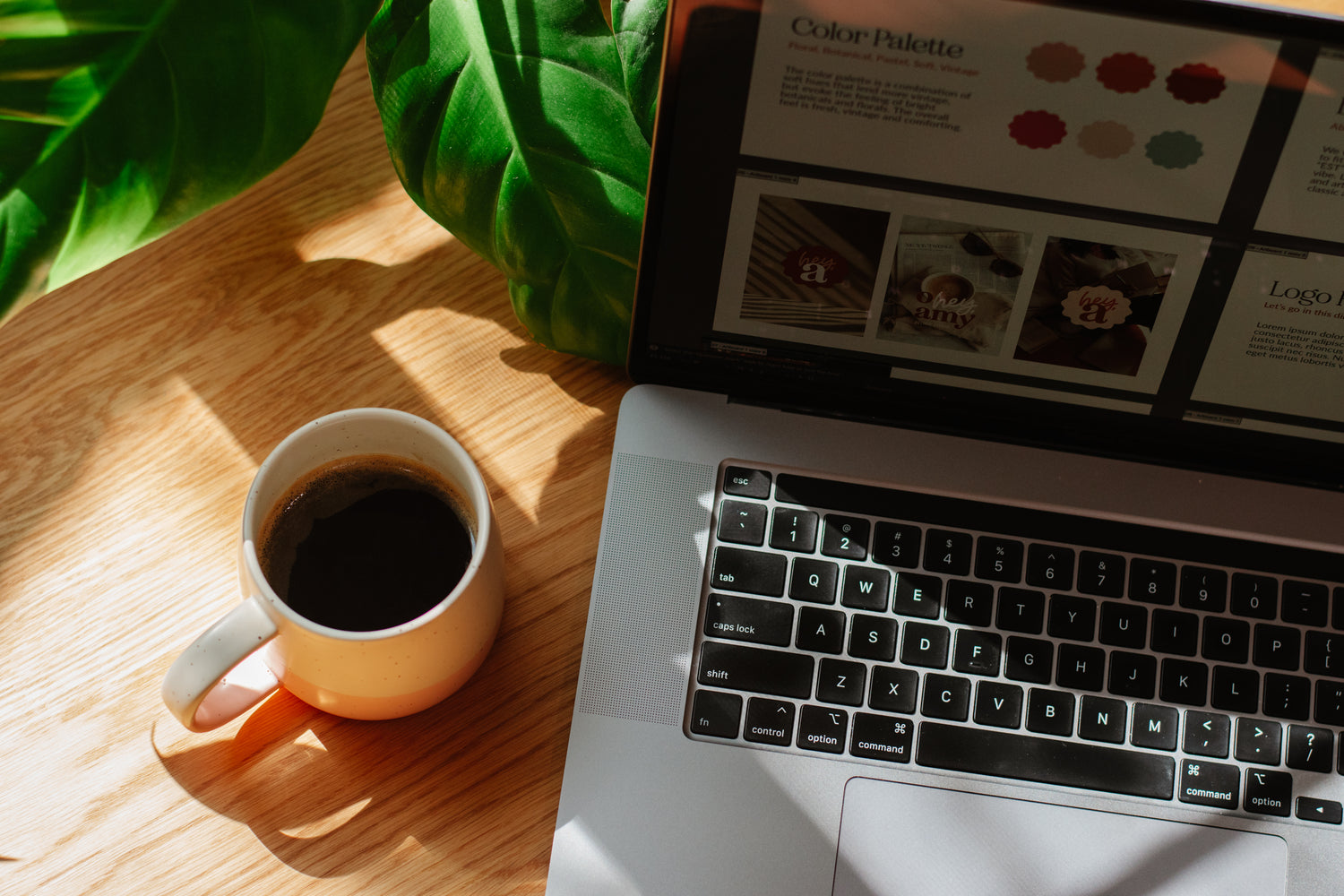 Laptop on a wooden table with a cup of coffee and green leaves