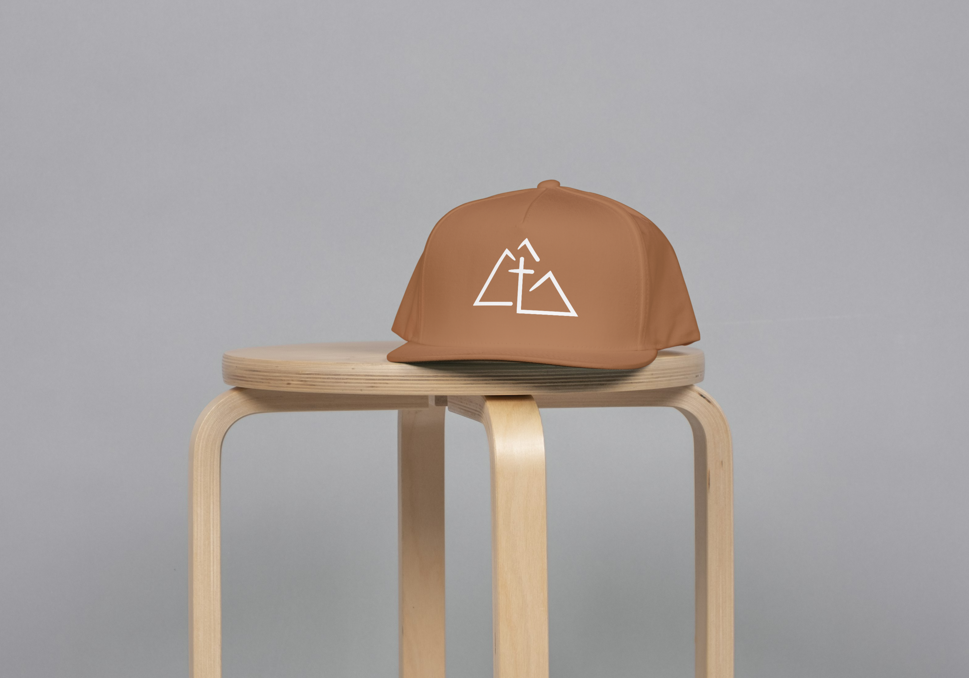 Brown cap with a white boulder valley christian logo on a wooden stool against a gray background
